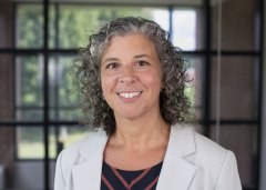 Donna Dolansky in light-colored blazer stands in front of window and smiles.